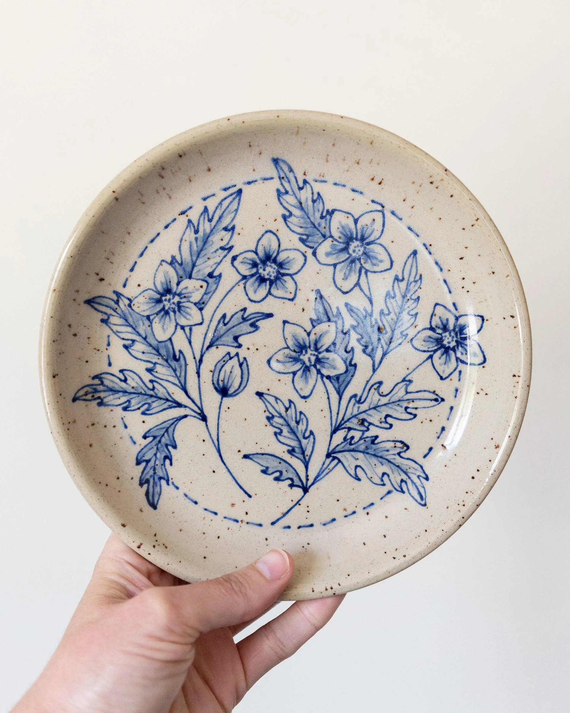 Hand holding a ceramic plate by Amy Brockman with blue floral design.