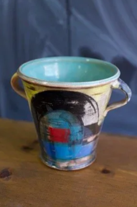Decorative ceramic mug with abstract painted design, placed on a wooden surface by Pedro Centeno