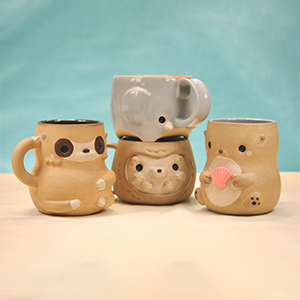 Four ceramic mugs with cute animal faces and designs, arranged on a surface with a teal background. - Glen Deiter