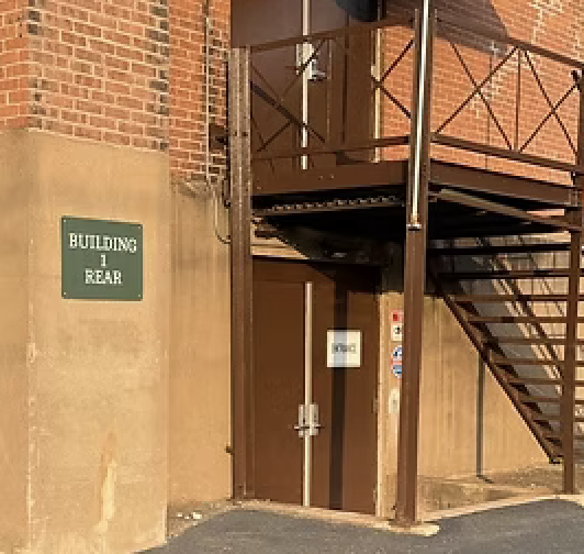 Back entrance of a building with a metal staircase and a green sign that reads 'Buttoning to Rear'.