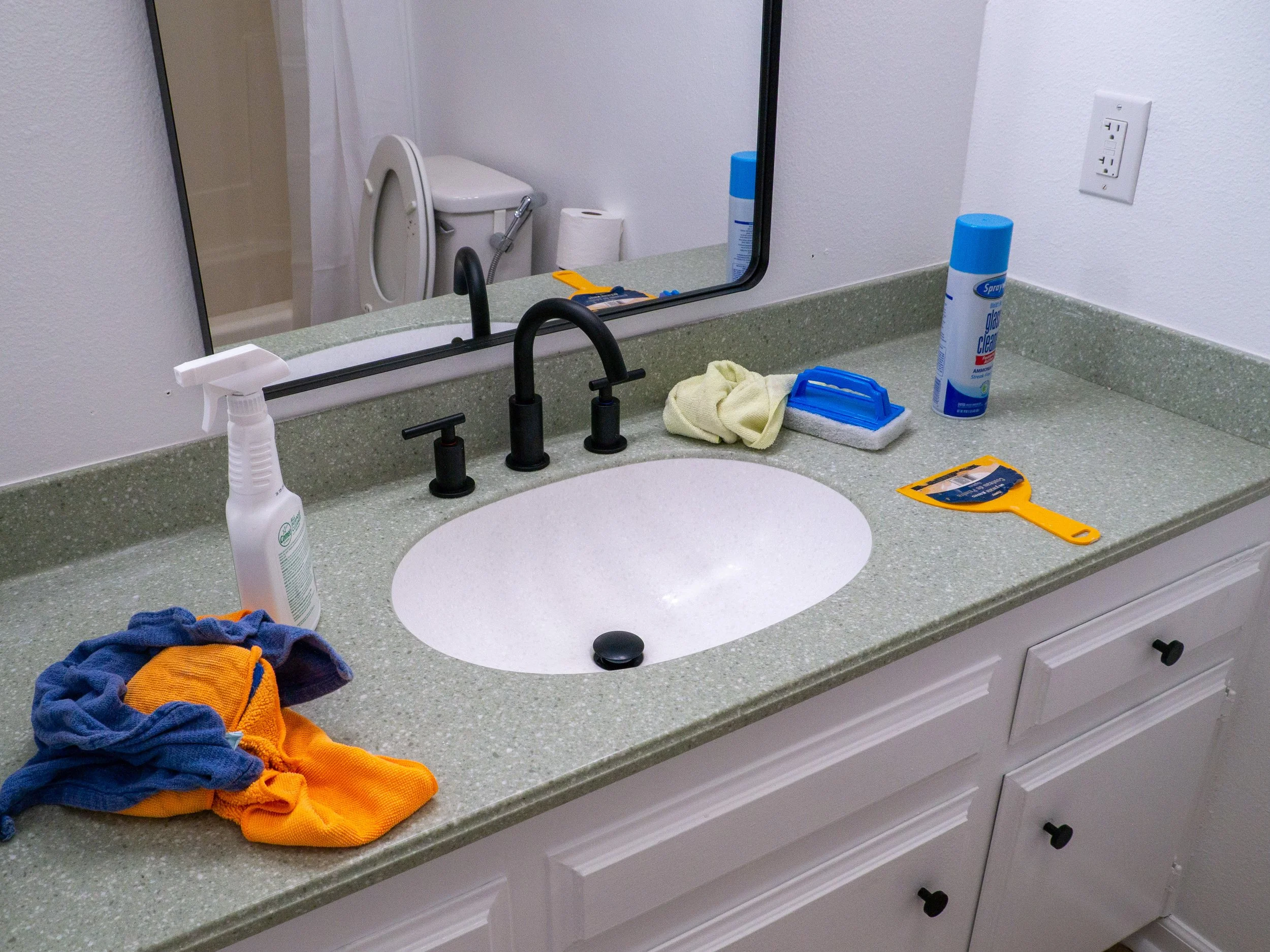 Bathroom vanity during a professional cleaning with cleaning products, cloths and tools arranged on the counter.