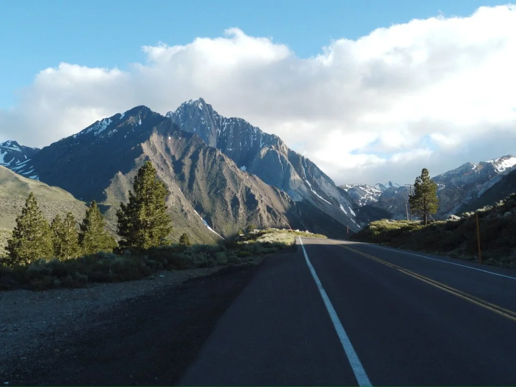 Scenic mountain road in Mammoth Lakes, California surrounded by pine trees and snow-covered peaks.