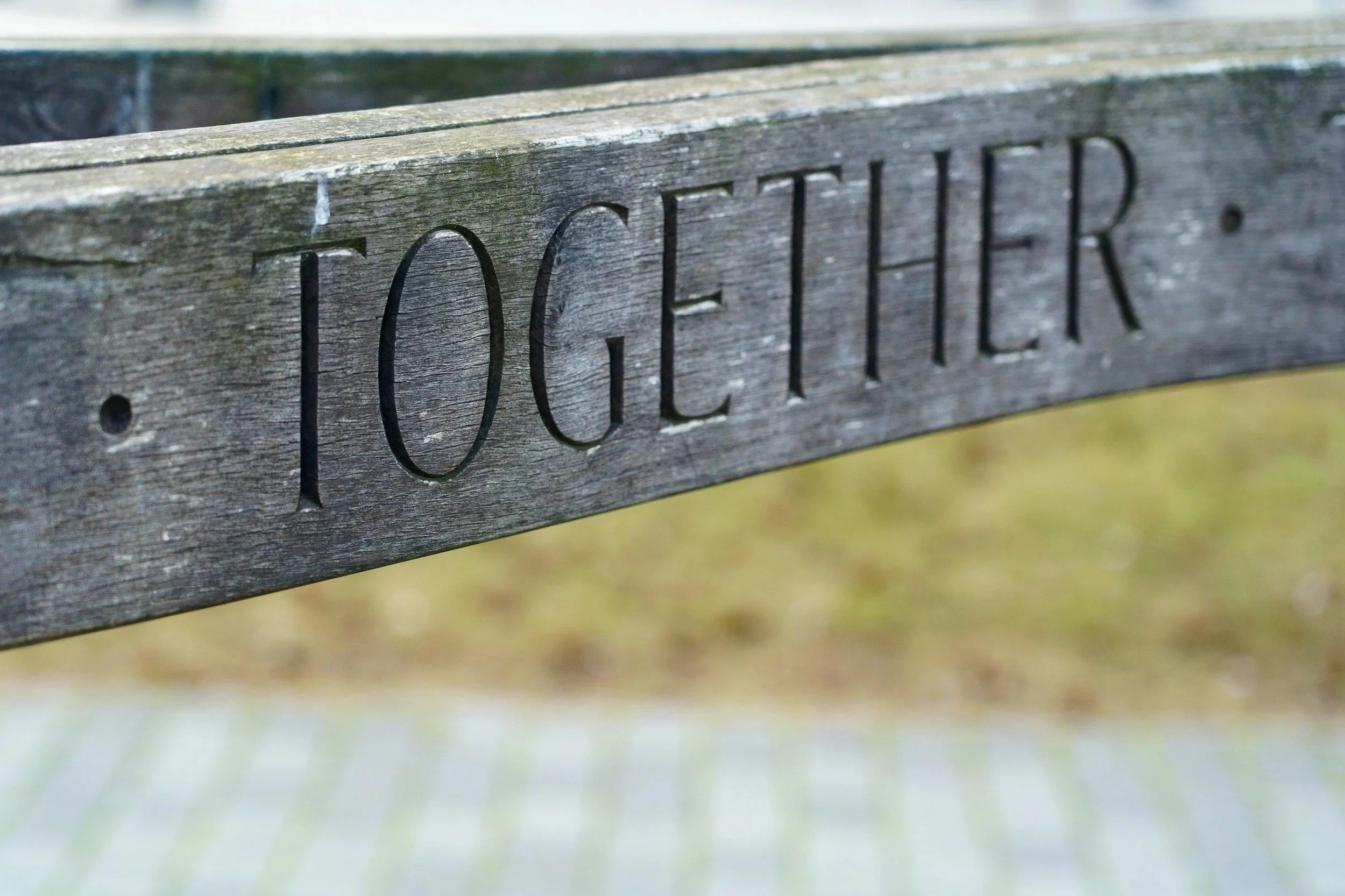 Close-up of a weathered wooden bench with the word 'FOOTER' carved into it, outdoors on a cloudy day.