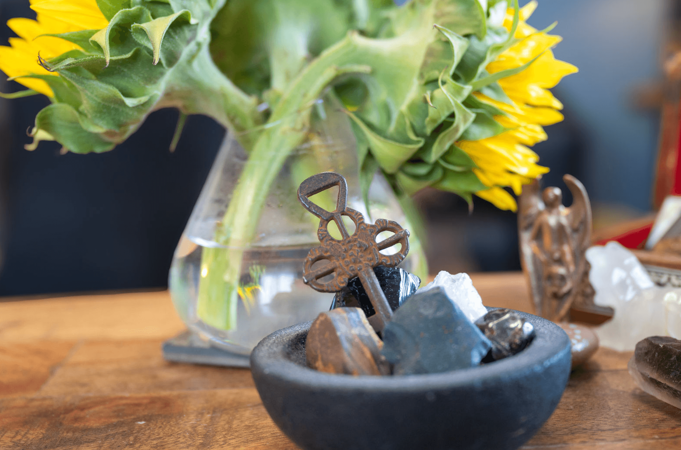 Close-up of a sunflower in a glass vase on a wooden surface, with small decorative objects and stones surrounding the vase.