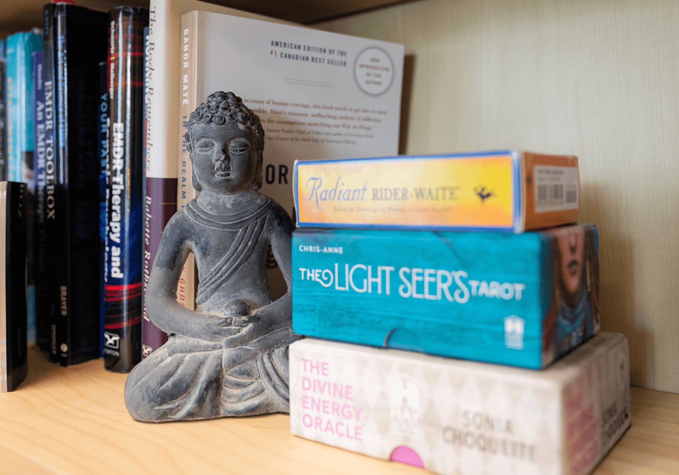 A wooden bookshelf with books, a gray Buddha statue, and a box of 'Radiant Rider-Waite' tarot cards.