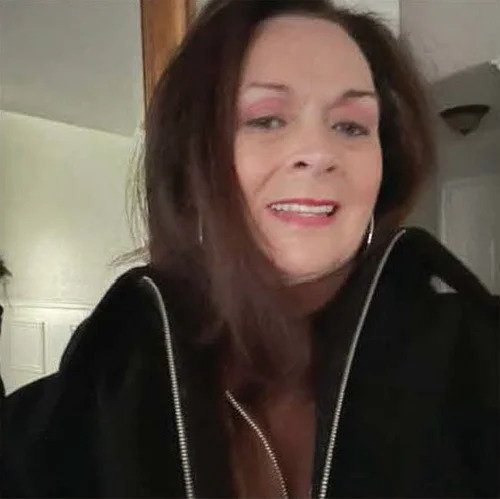 A woman with shoulder-length dark hair, wearing makeup and a black jacket, smiling at the camera.