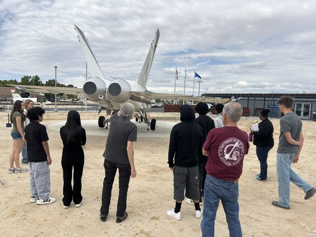 Group of people observing a F/A-18 fighter jet aircraft on display outdoors at the China Lake museum