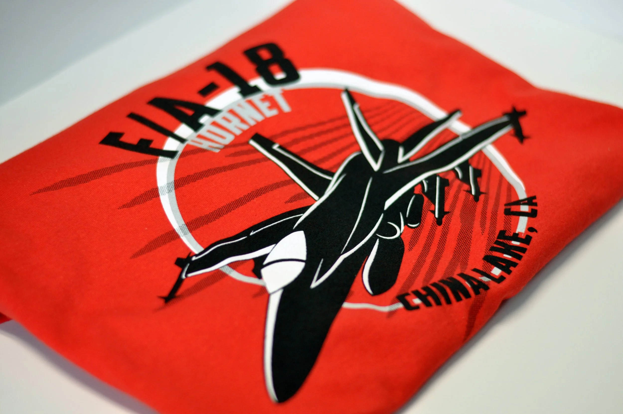 Close-up of a red shirt with a black and white graphic logo and black text reading "F/A-18 Hornet".