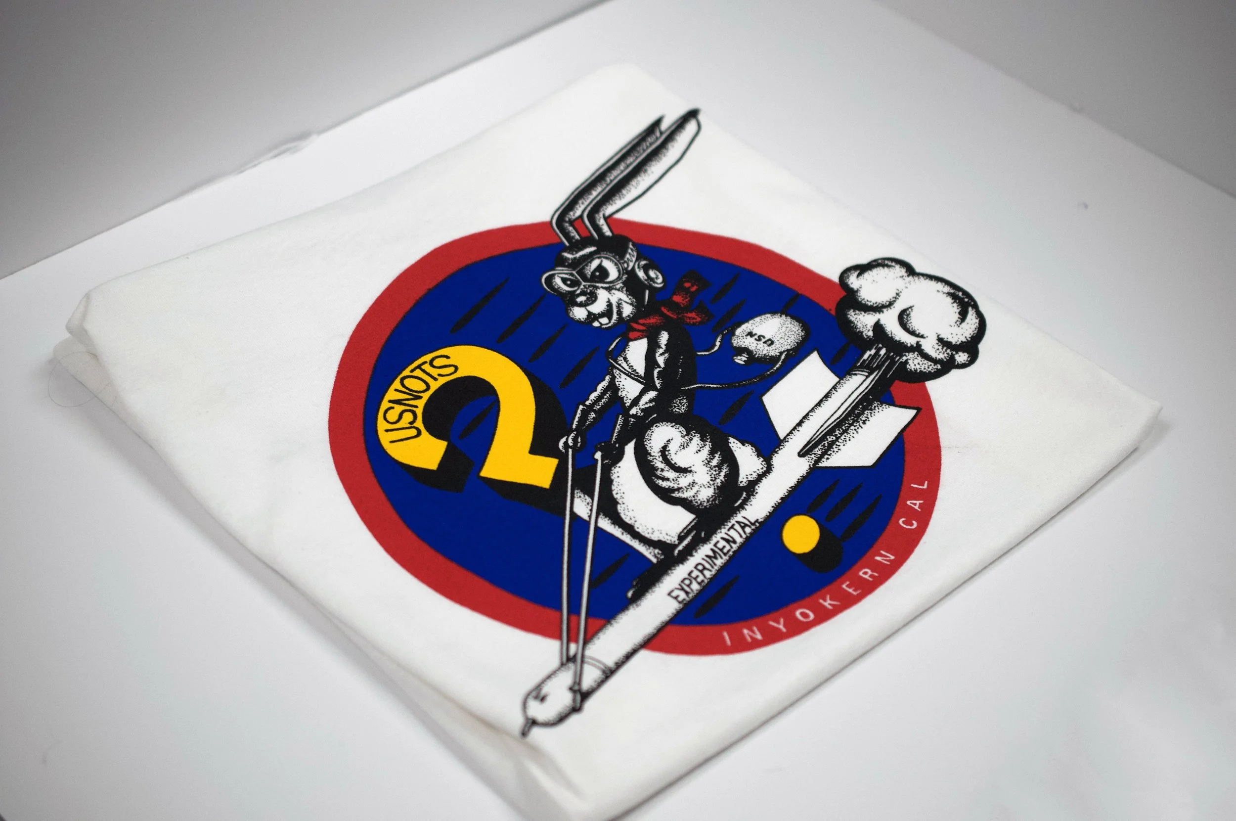 Close-up of a printed fabric with a graphic design featuring a cartoon jack rabbit riding a missile, set against a circular red and blue background with yellow text reading 'NOTS'.