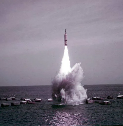 A Polaris missile launching from the water with a large splash and smoke cloud underneath.