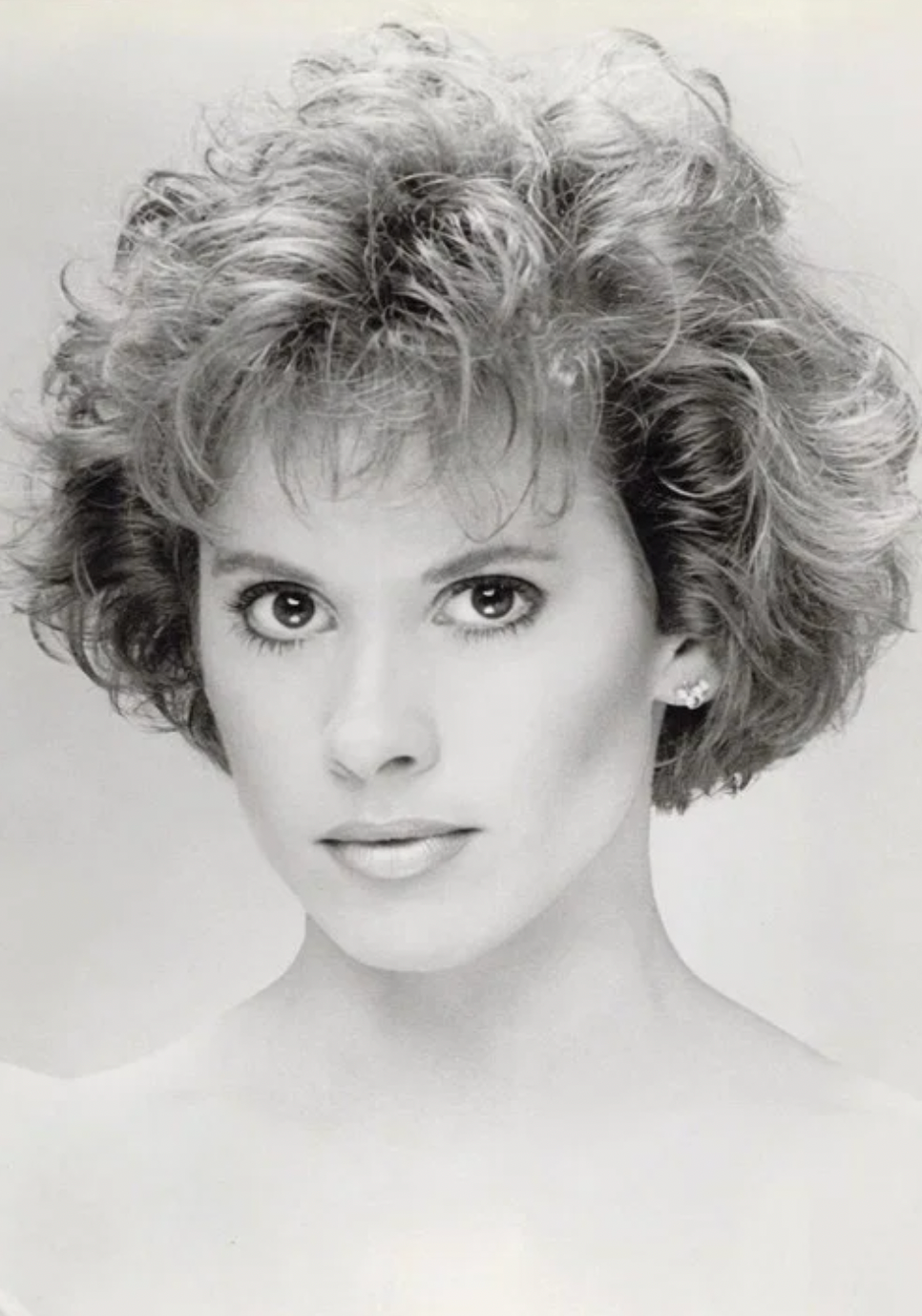 Black and white portrait of a woman with curly hair, large eyes, and a confident expression.
