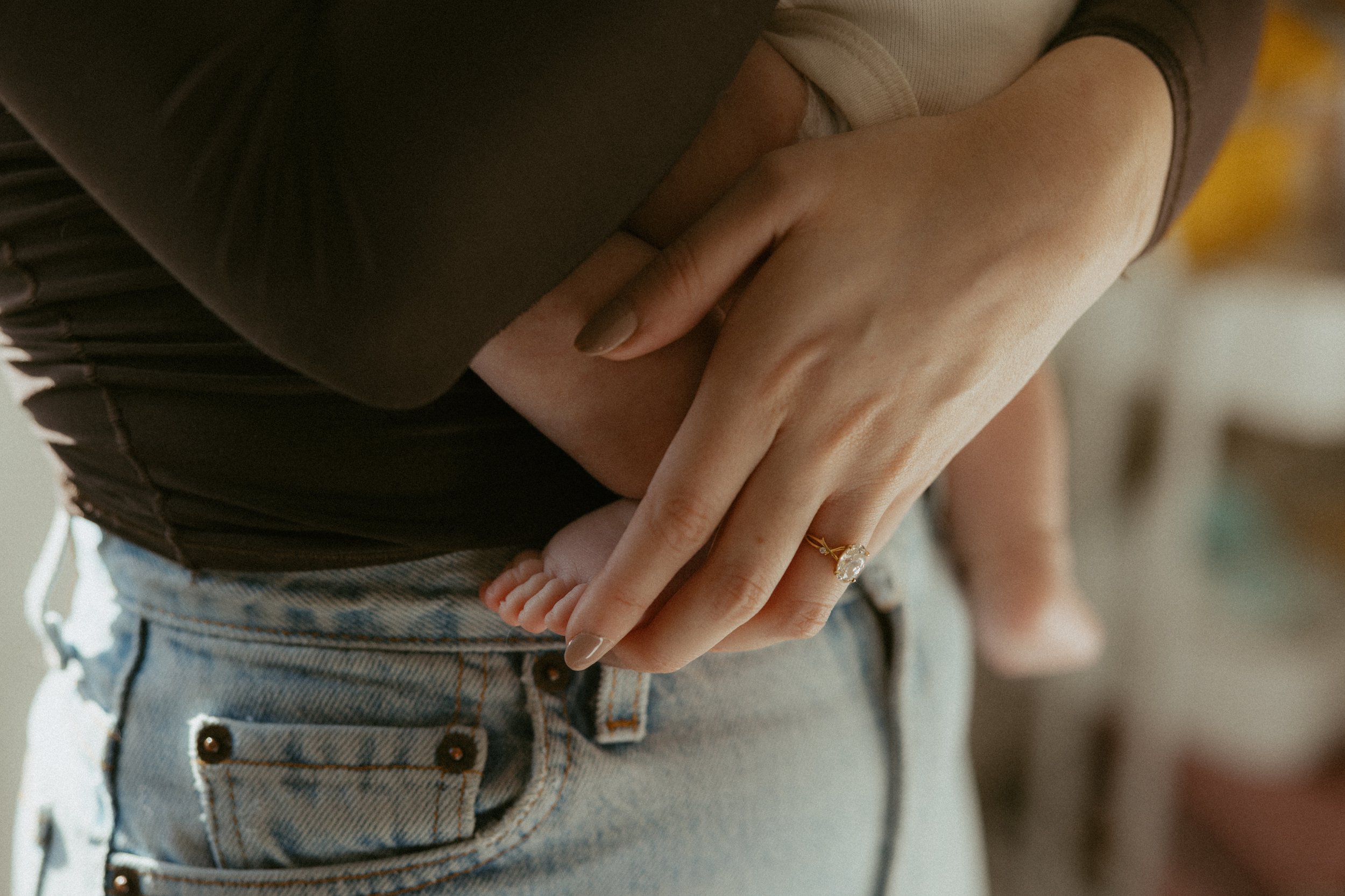 Close-up of a person holding a baby's hand, wearing a ring, with both people dressed casually.