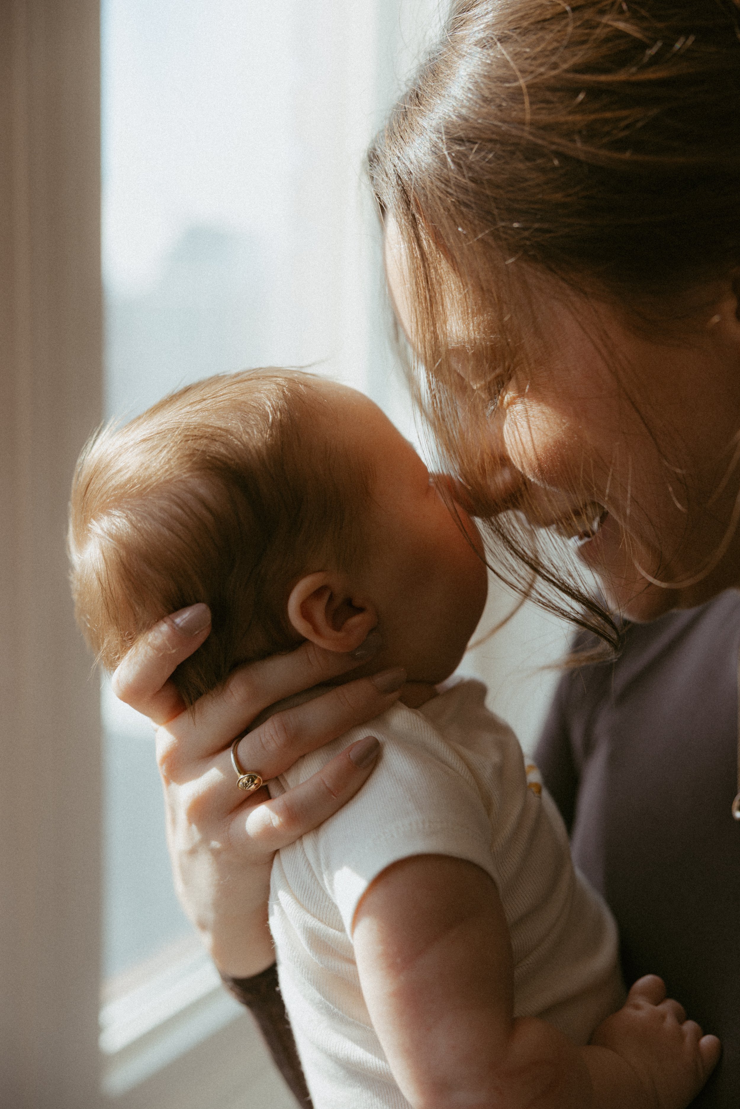 A woman with long, brown hair holding a young child with short, blonde hair close to her face, in a warmly lit room.