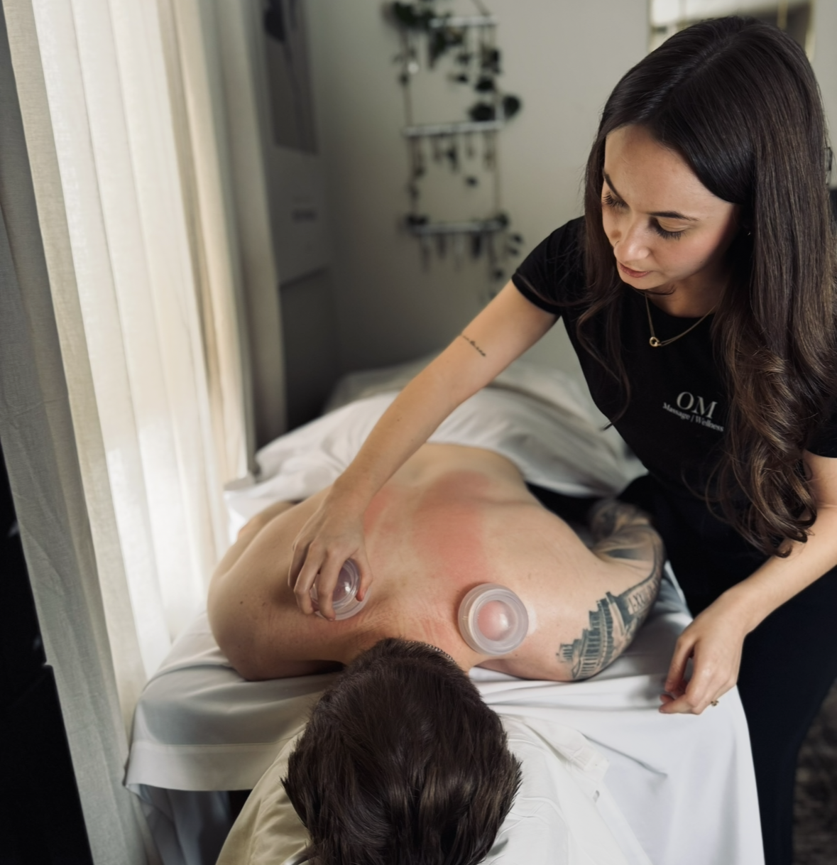 A woman receives a cupping therapy massage on her back from a therapist in a clinic setting.