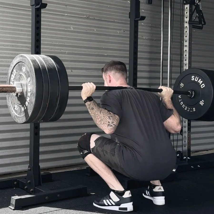 Man squatting while lifting a barbell loaded with multiple weight plates in a gym.