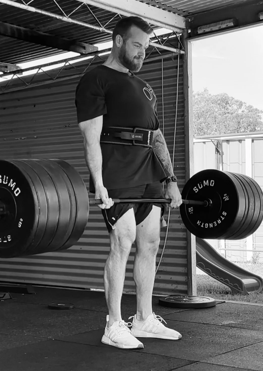 A man lifting a barbell with heavy weights at a gym, wearing a weightlifting belt and workout clothes.