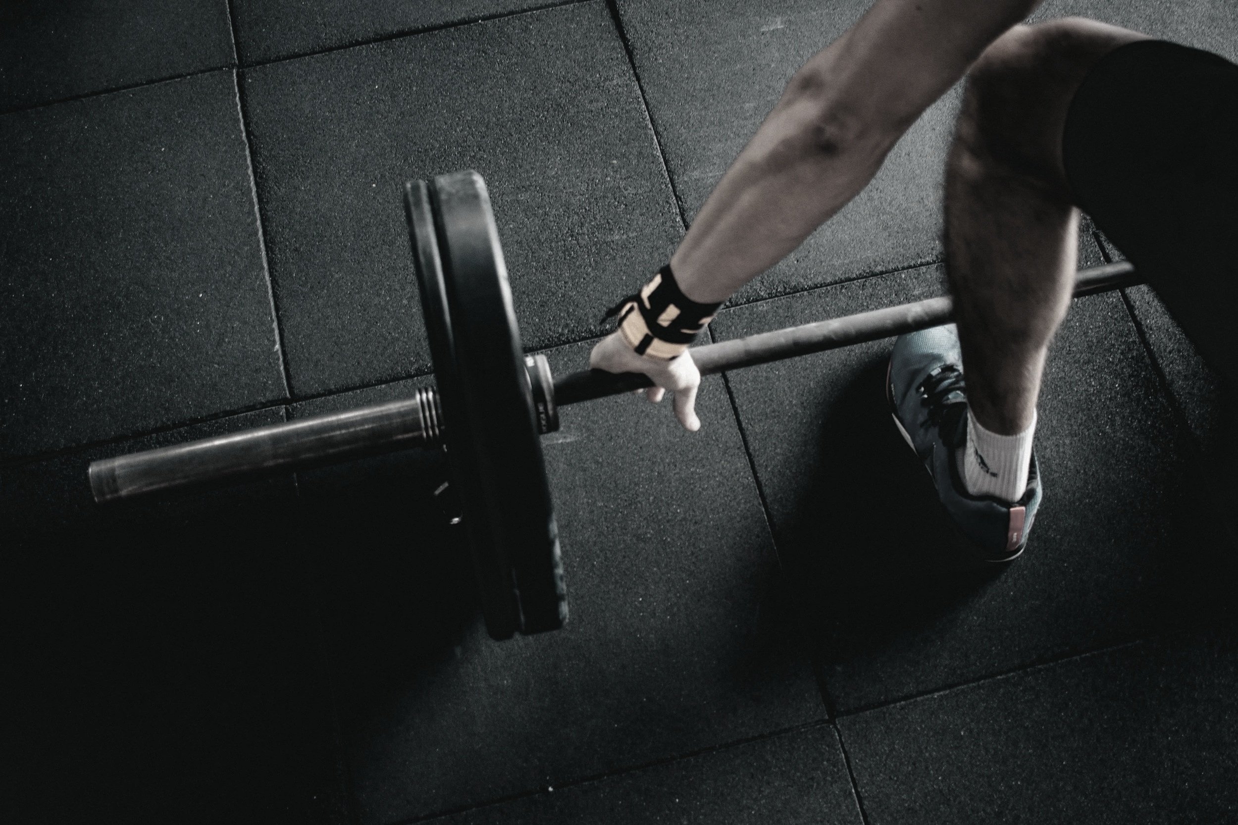 Person lifting a barbell during a workout in a gym with black rubber flooring.