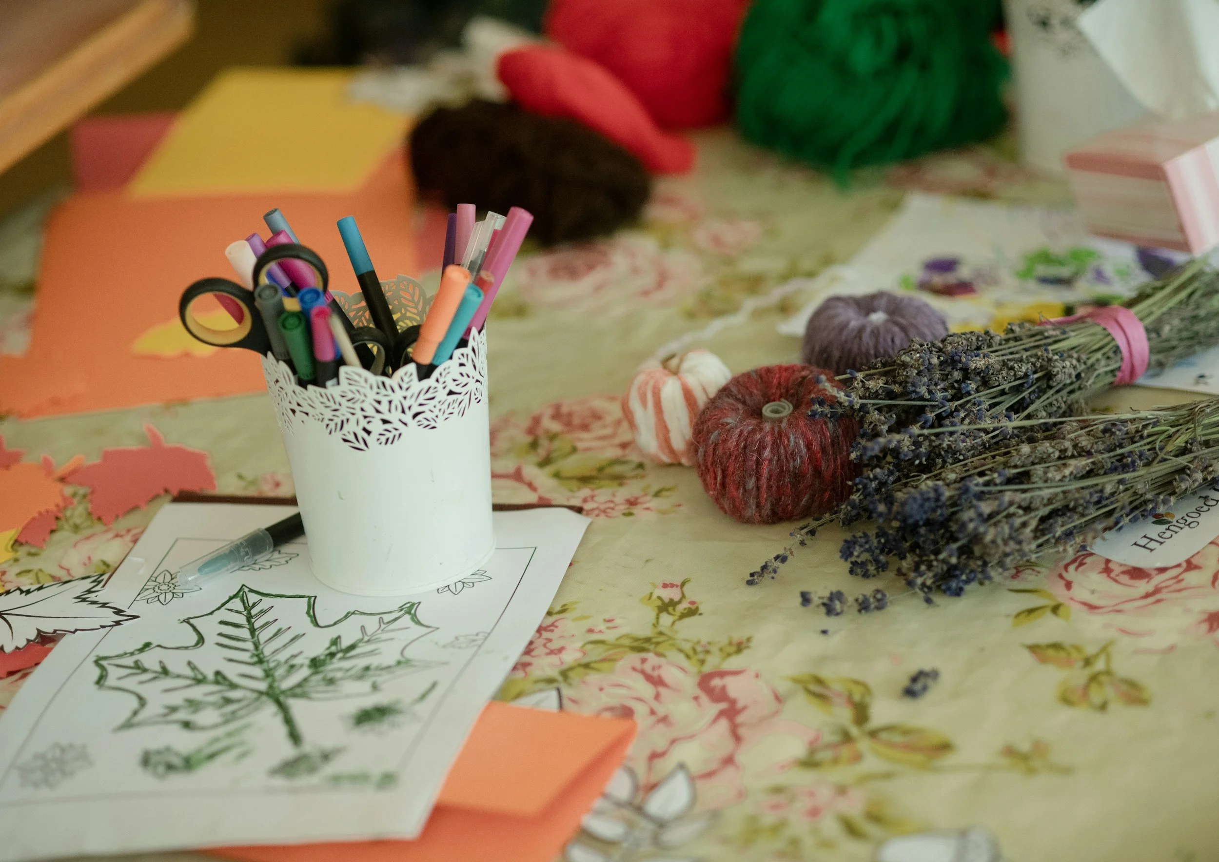 Craft supplies including colored markers, colored paper, dried lavender, and holiday-themed coloring pages on a table.