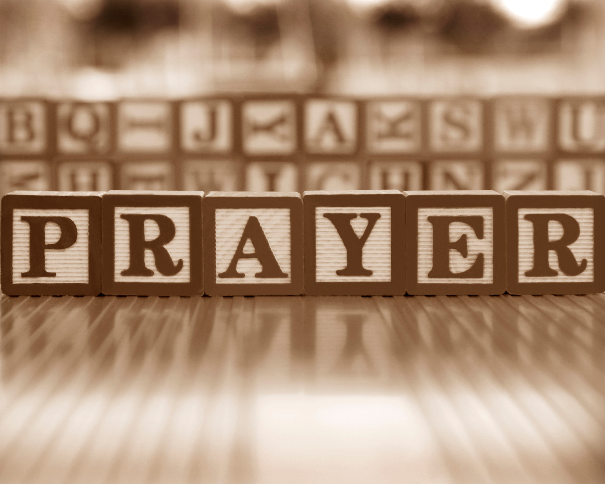 Close-up photograph of wooden alphabet blocks spelling the word 'PRAYER' on a light-colored surface with a blurred background.