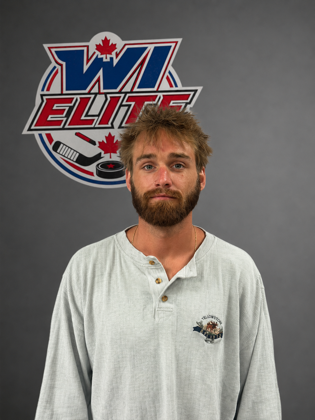 A man with a beard and messy hair stands in front of a gray background with a 'WL Elite' logo featuring a hockey stick, puck, and Canadian maple leaf.