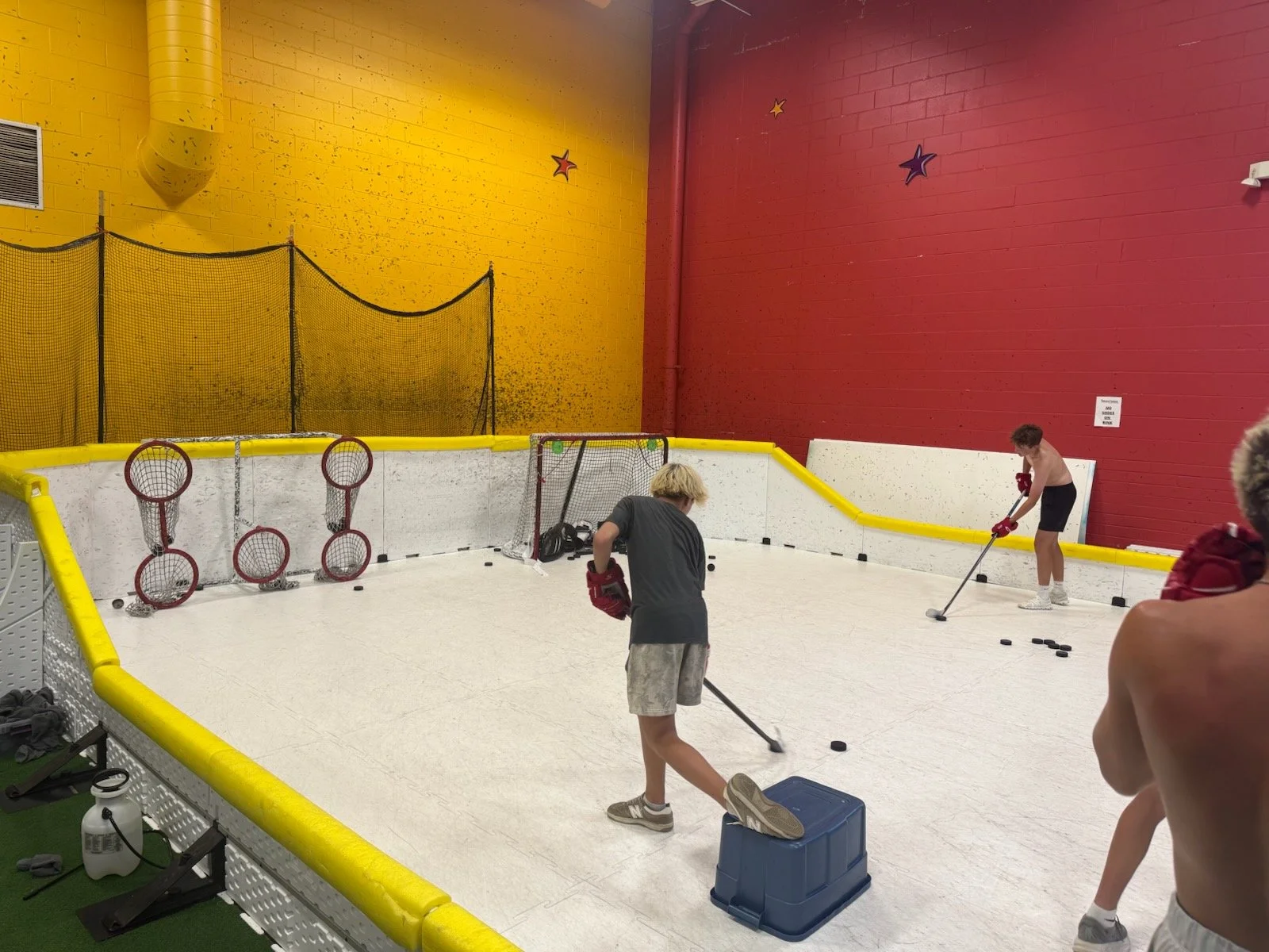 People practicing hockey skills in an indoor hockey rink with red and yellow walls and star decorations.