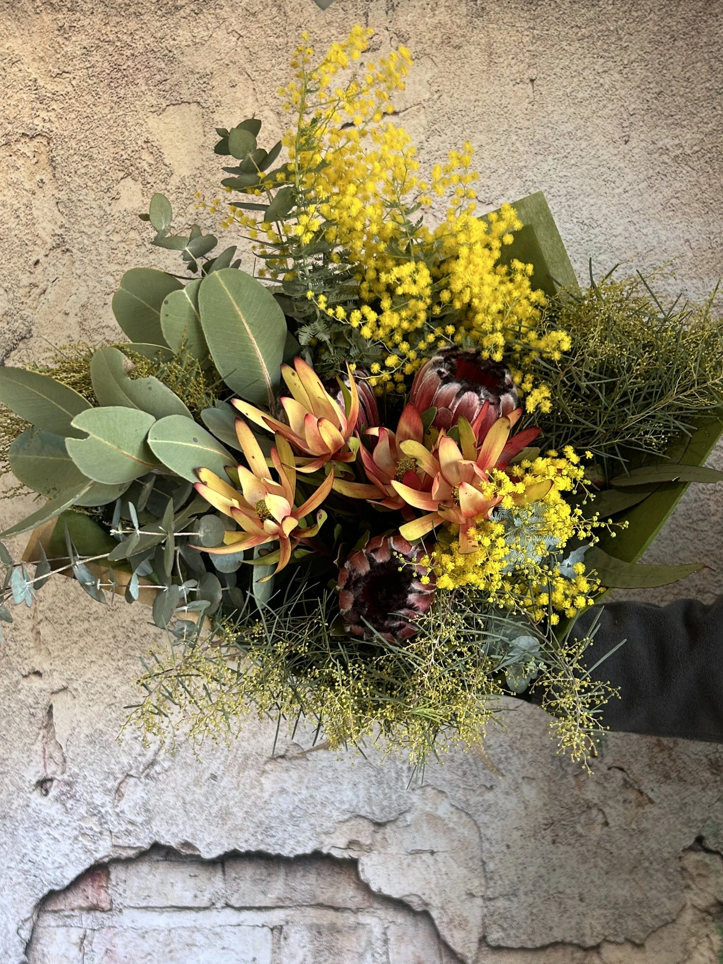 A bouquet of yellow, red, and green flowers and foliage resting on a rough stone surface.