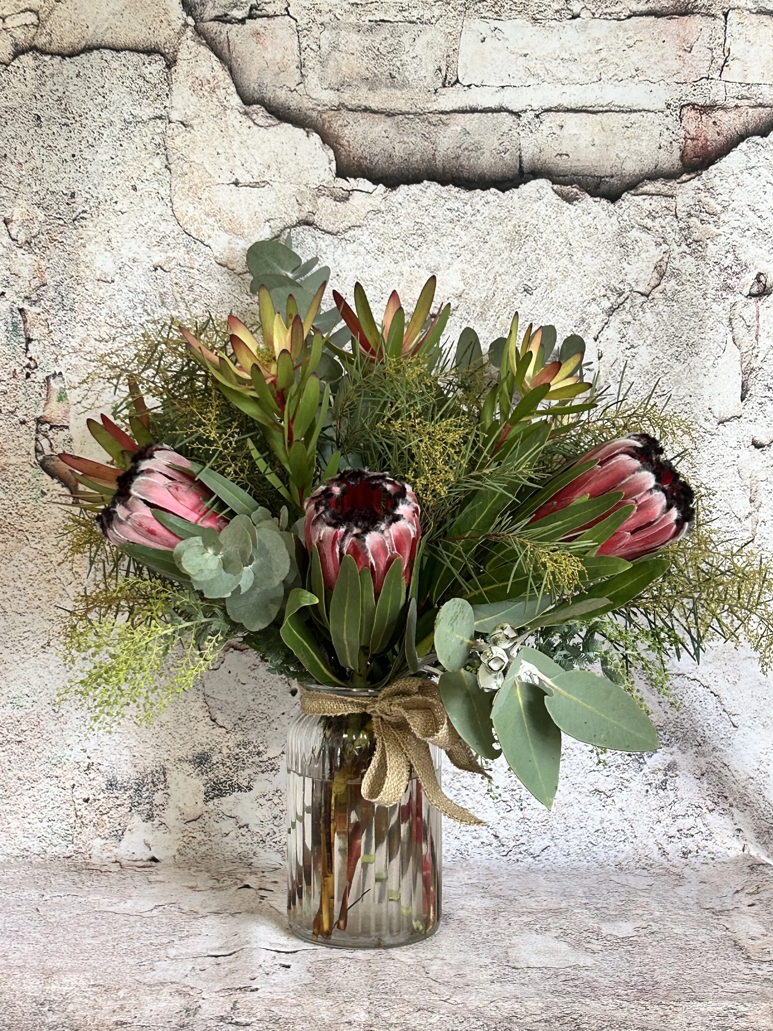 A glass vase filled with a floral arrangement of flowers and green foliage is placed on a textured stone surface.