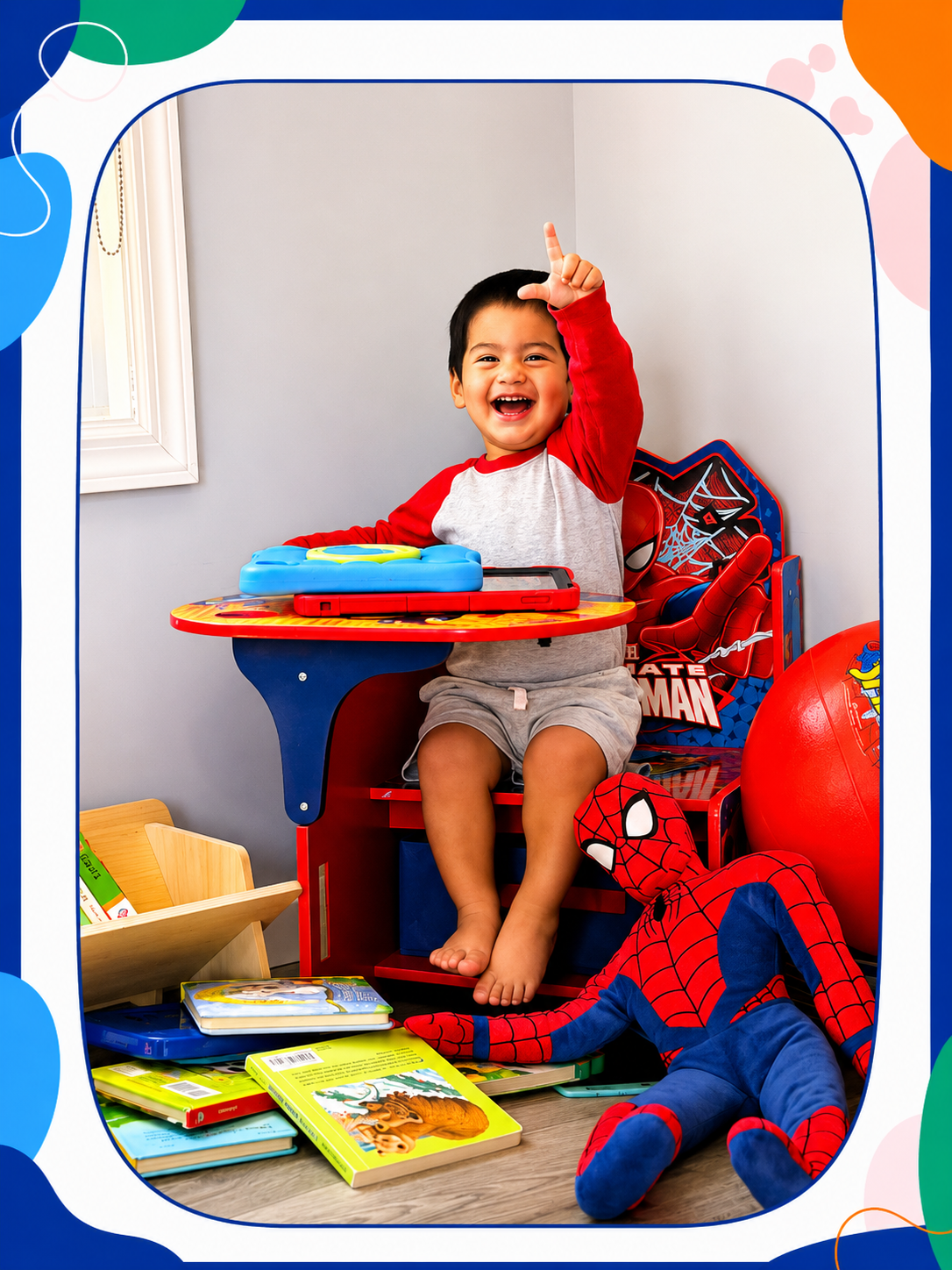 A young boy sitting at a toy table, smiling and pointing upward, surrounded by Spider-Man themed toys and books.