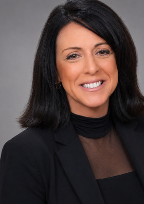 A woman with shoulder-length black hair smiling, wearing a black blazer and top, against a gray background.