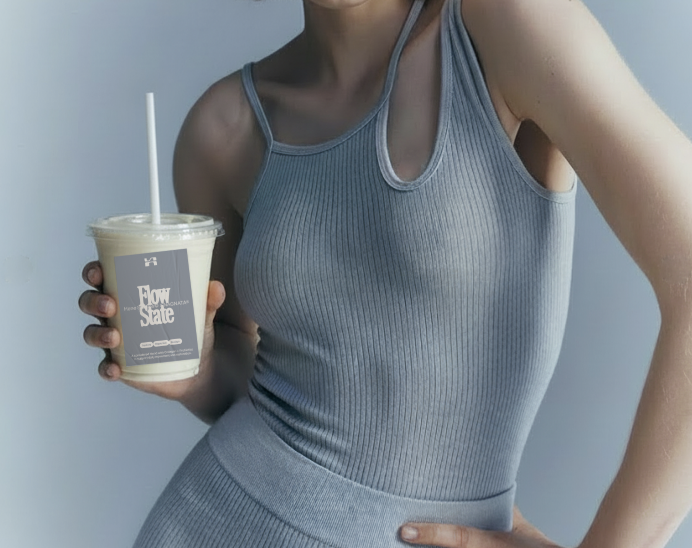 A woman in a light gray athletic outfit holding a smoothie with a straw, with a sticker that says 'Flow State' on the cup.