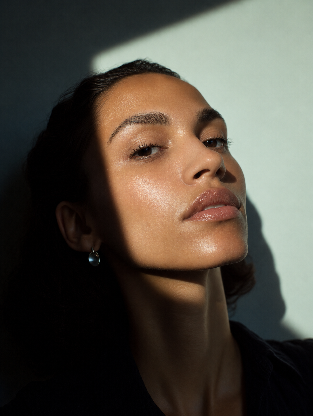Close-up of a woman's face with natural makeup, illuminated by sunlight, with shadow across part of her face.
