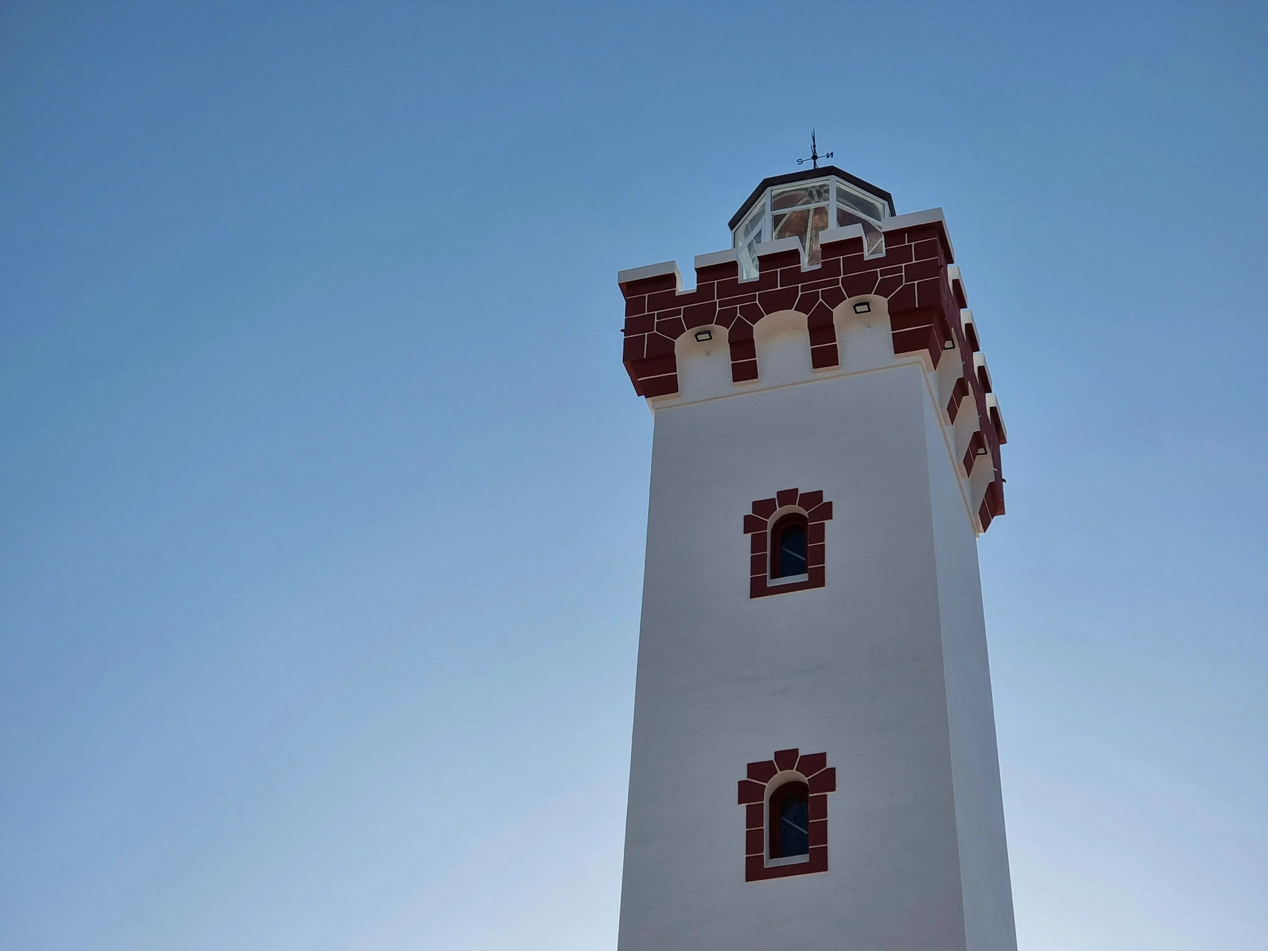Torre de faro con estructura blanca y detalles de ladrillo rojo, contra un cielo despejado.