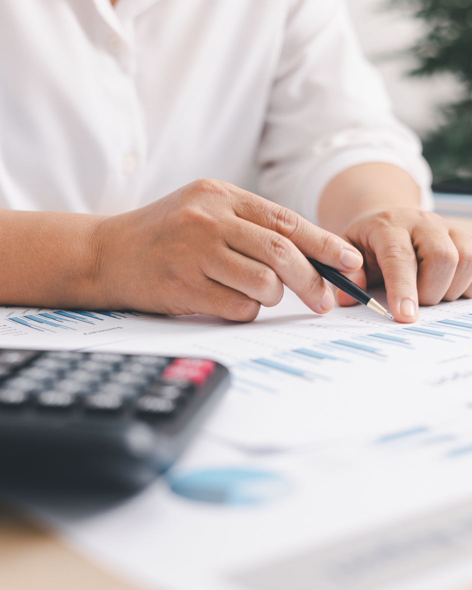 Person in a white shirt analyzing financial documents with a pen, calculator, and charts on the table.