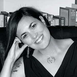 A woman with dark hair smiling at the camera, sitting in front of a bookshelf.