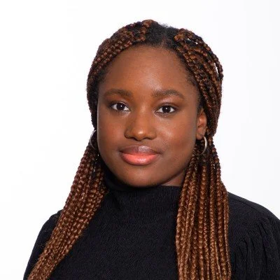 Jeune femme noire avec des tresses brunes portant un pull noir, regardant vers l'avant, fond blanc.