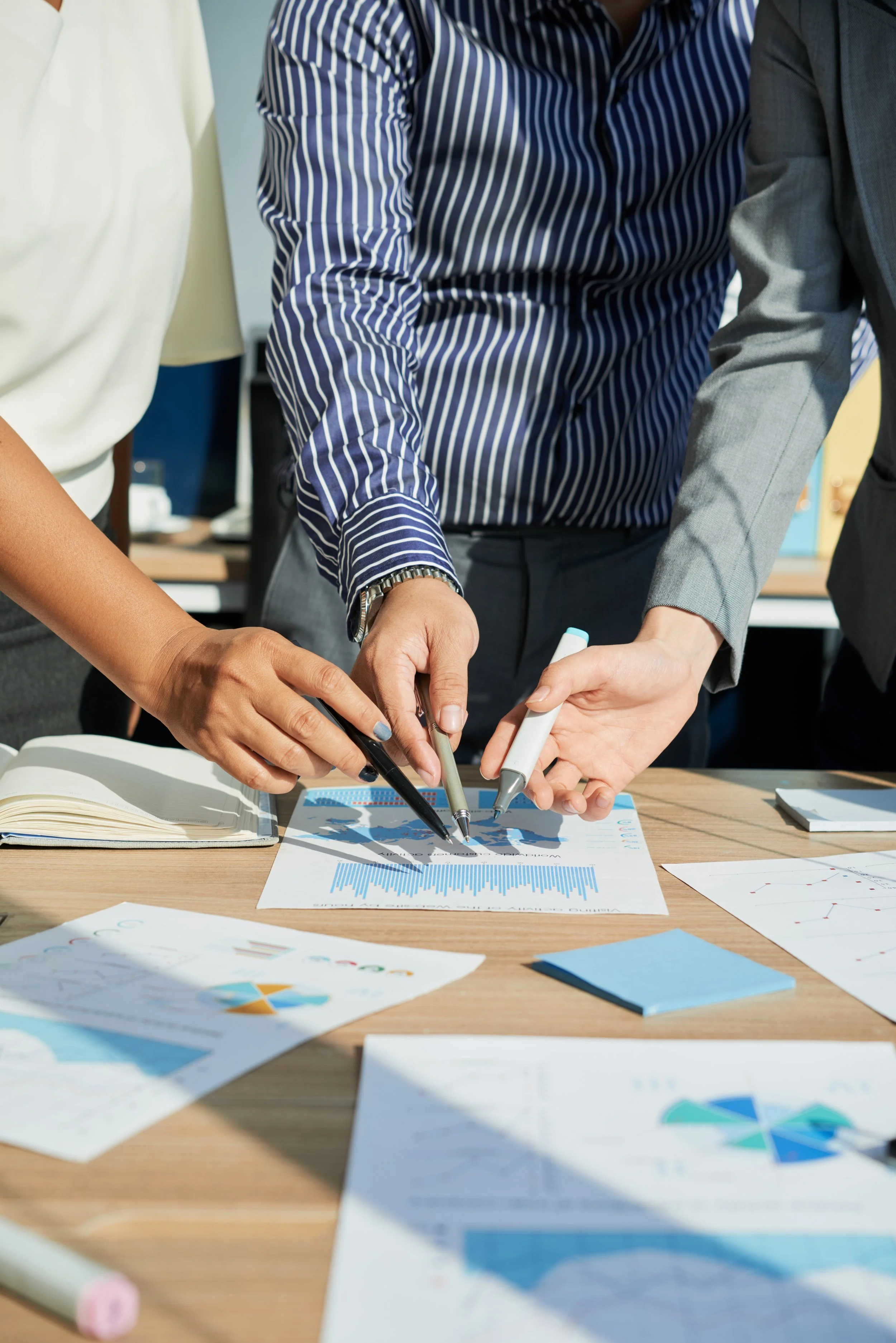 Several people are gathered around a table, working on printed charts and graphs with markers. They are collaborating on data analysis in a professional office setting.
