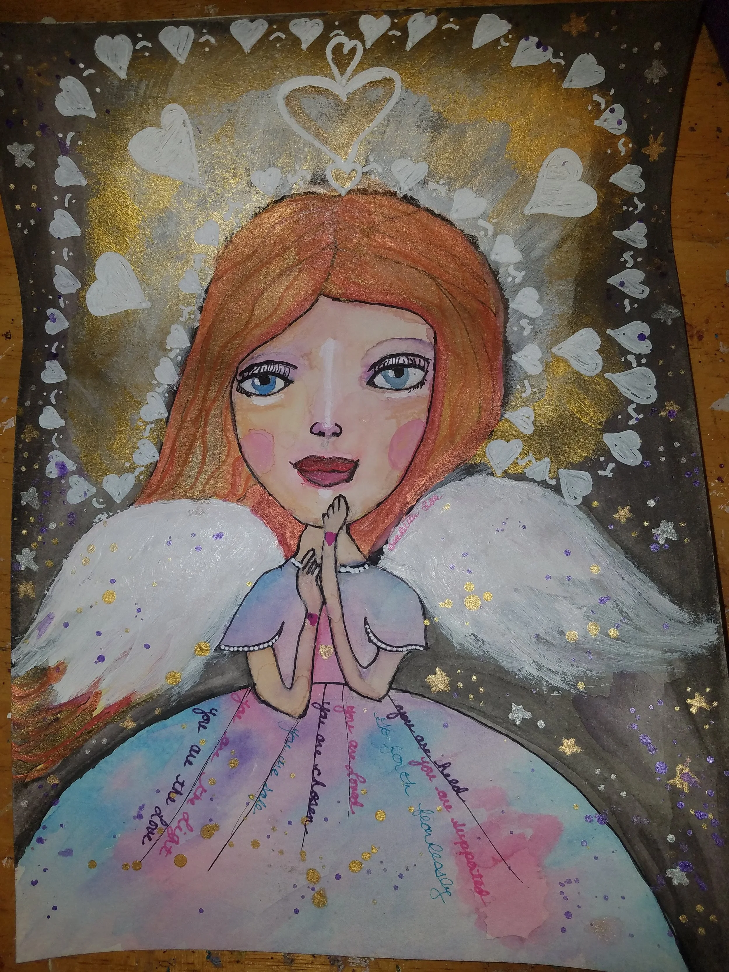 Handmade artwork of a girl with blue eyes and long hair with a gold, silver, and white background, surrounded by white hearts and golden stars, with handwritten colorful words on her dress and flowing downward.