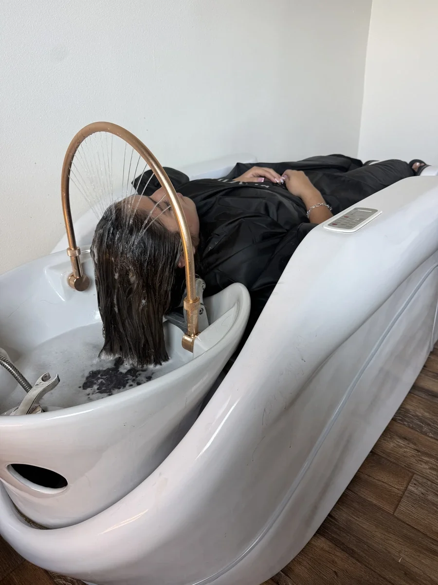 Client relaxing in a full-body massage shampoo bed during a Head Spa treatment at The Hair Court in Bryan-College Station, TX.