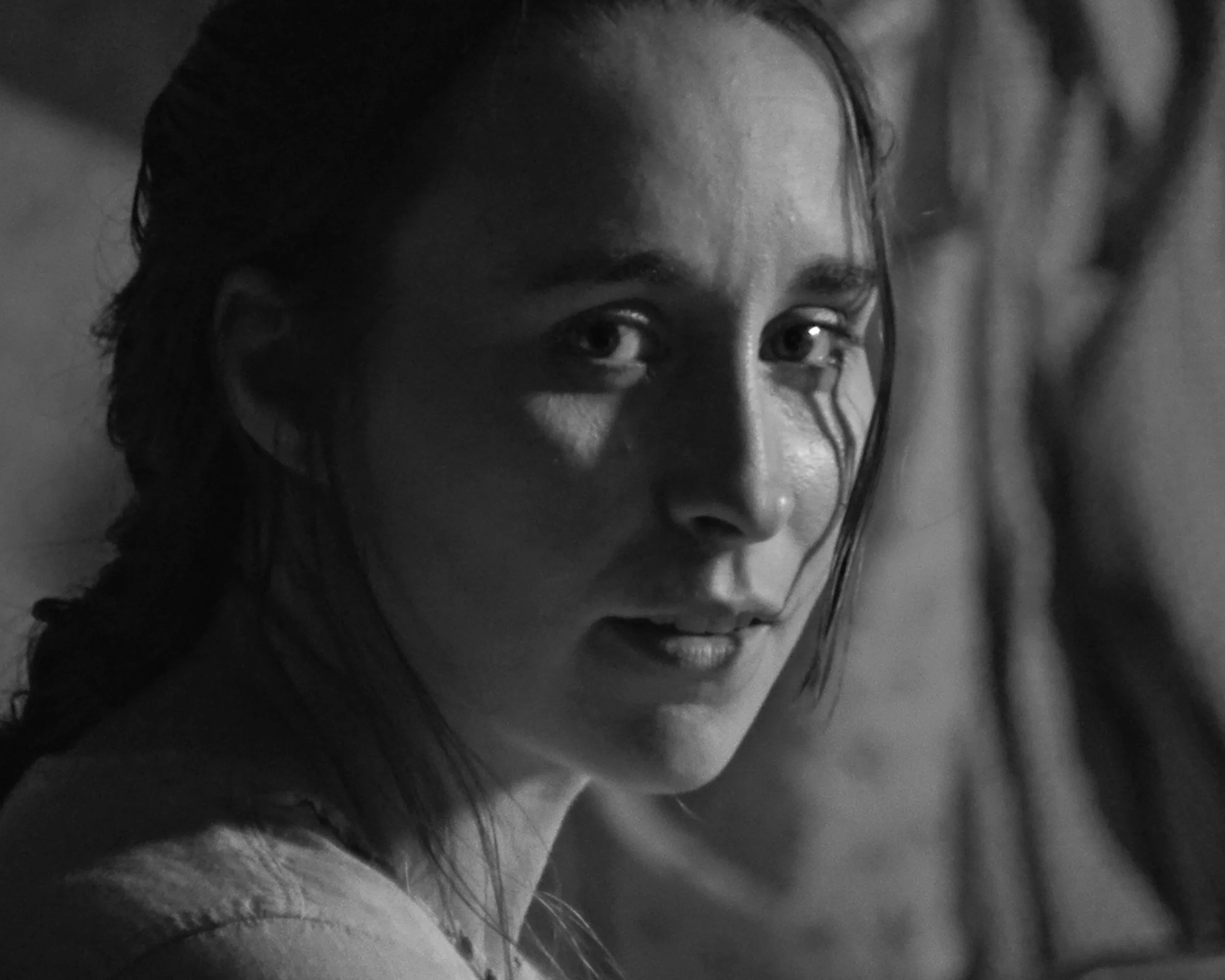 Close-up of a woman's face with dark hair, partially reflected in a mirror, in black and white.