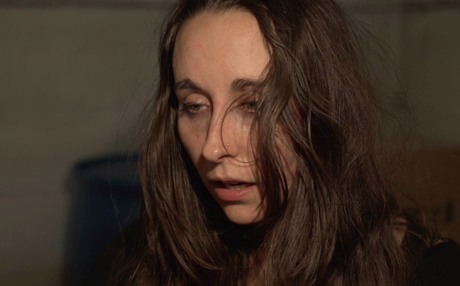 Close-up of a woman with long brown hair, looking down and to her right, with a neutral expression.