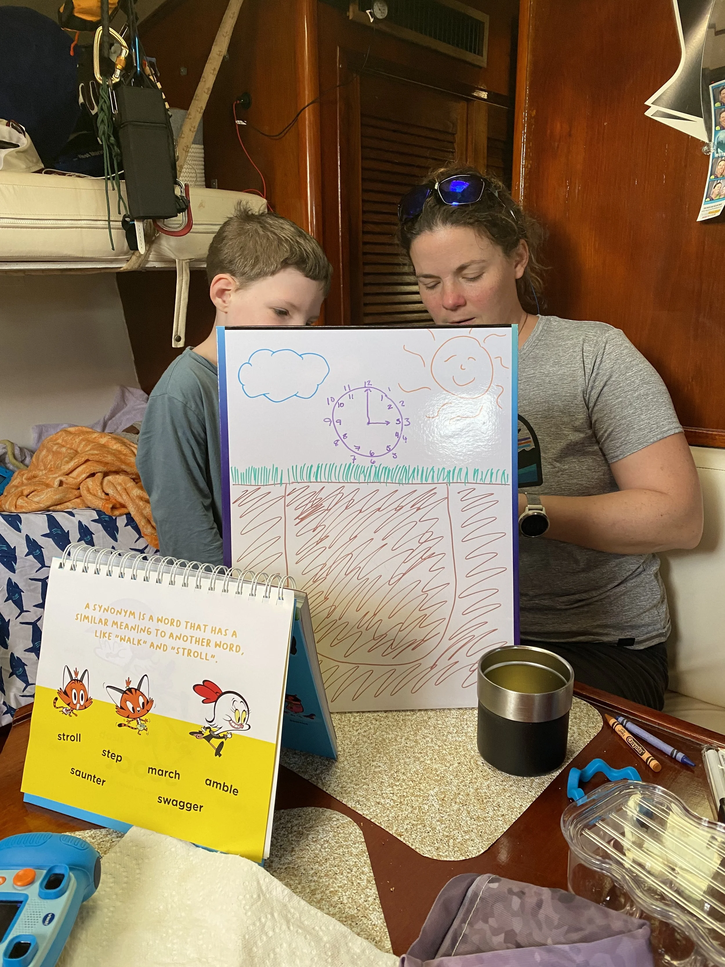 A boy and mom work on a dry erase board during homeschool time in a sailboat.