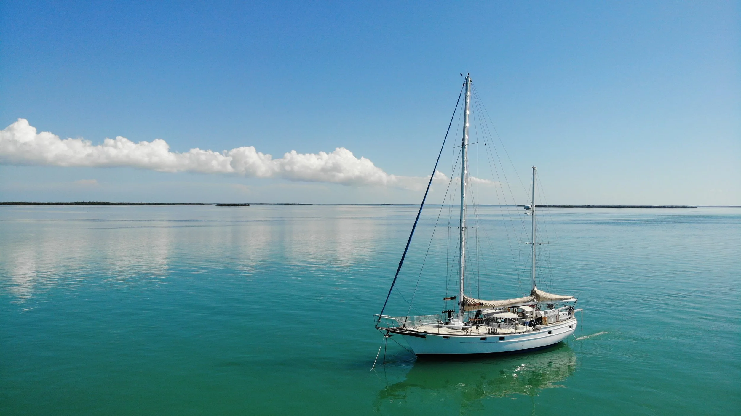 A sailboat anchored alone in calm turquoise water under a clear sky.