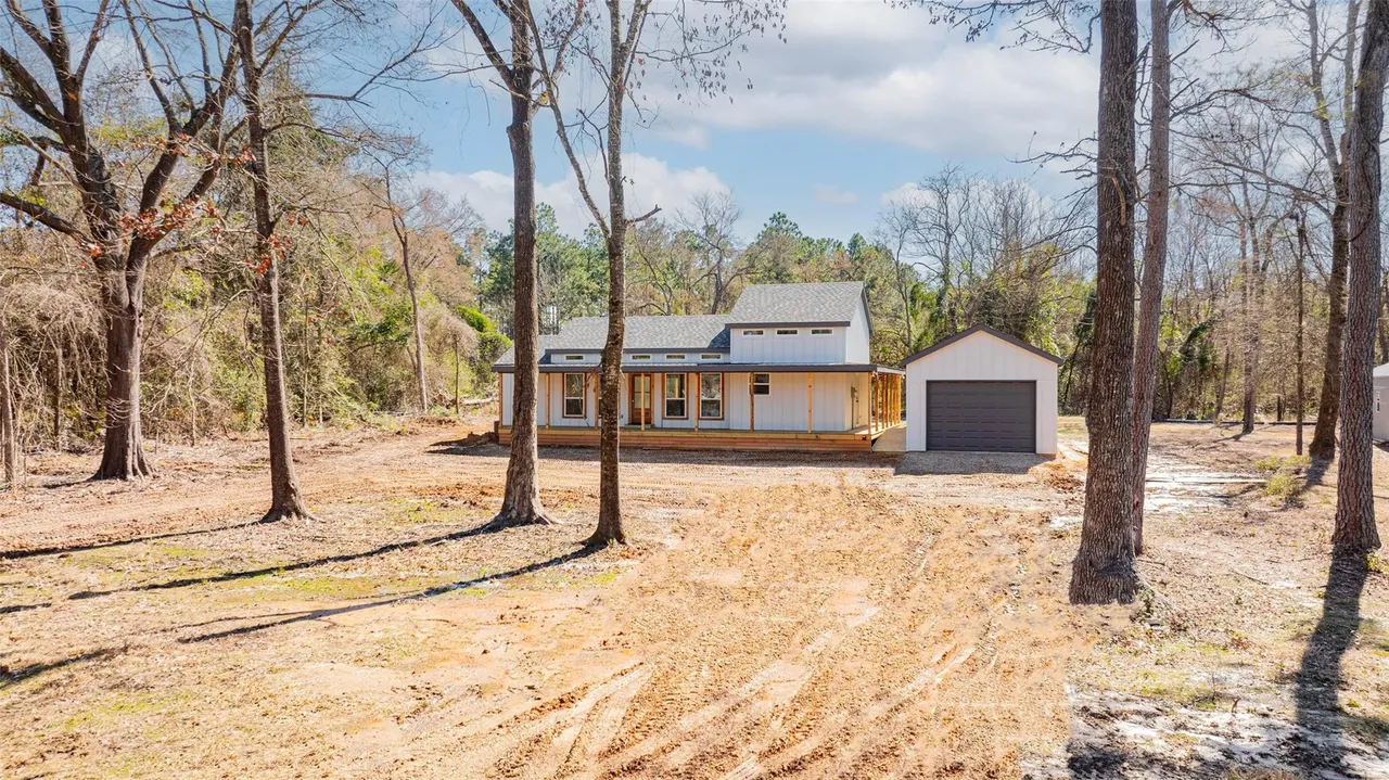 A house under construction in a wooded area with cleared land and trees around.