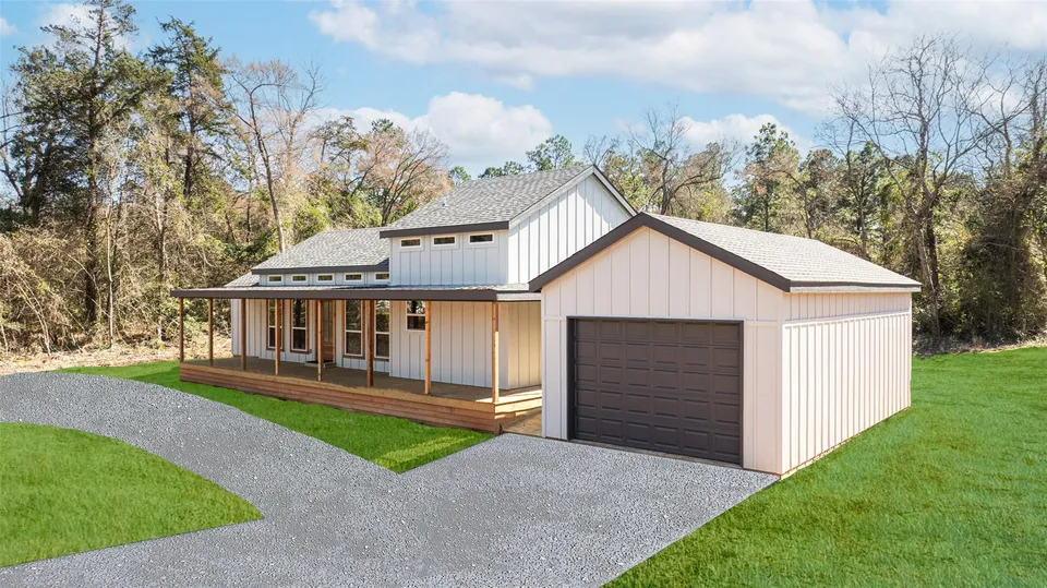 Newly built modern farmhouse with a covered porch, attached garage, white siding, and a gray metal roof, set in a green yard with a gravel driveway and wooded background.