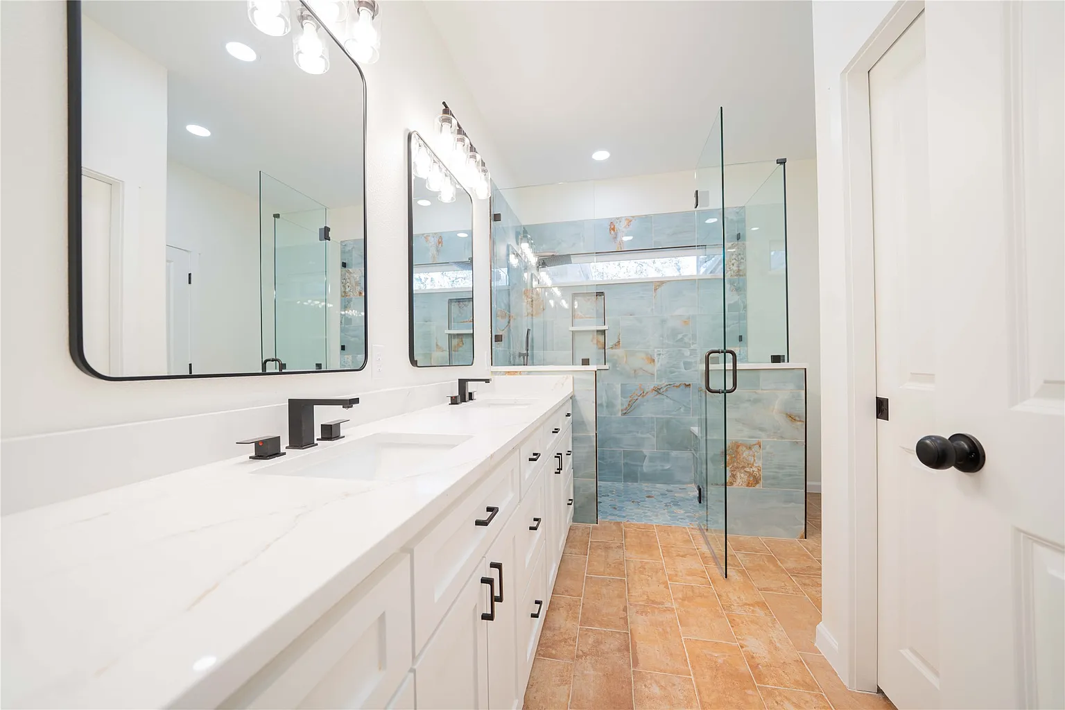 Modern bathroom with double vanity, large mirrors, black fixtures, and a glass-enclosed walk-in shower with blue and orange tile accents.
