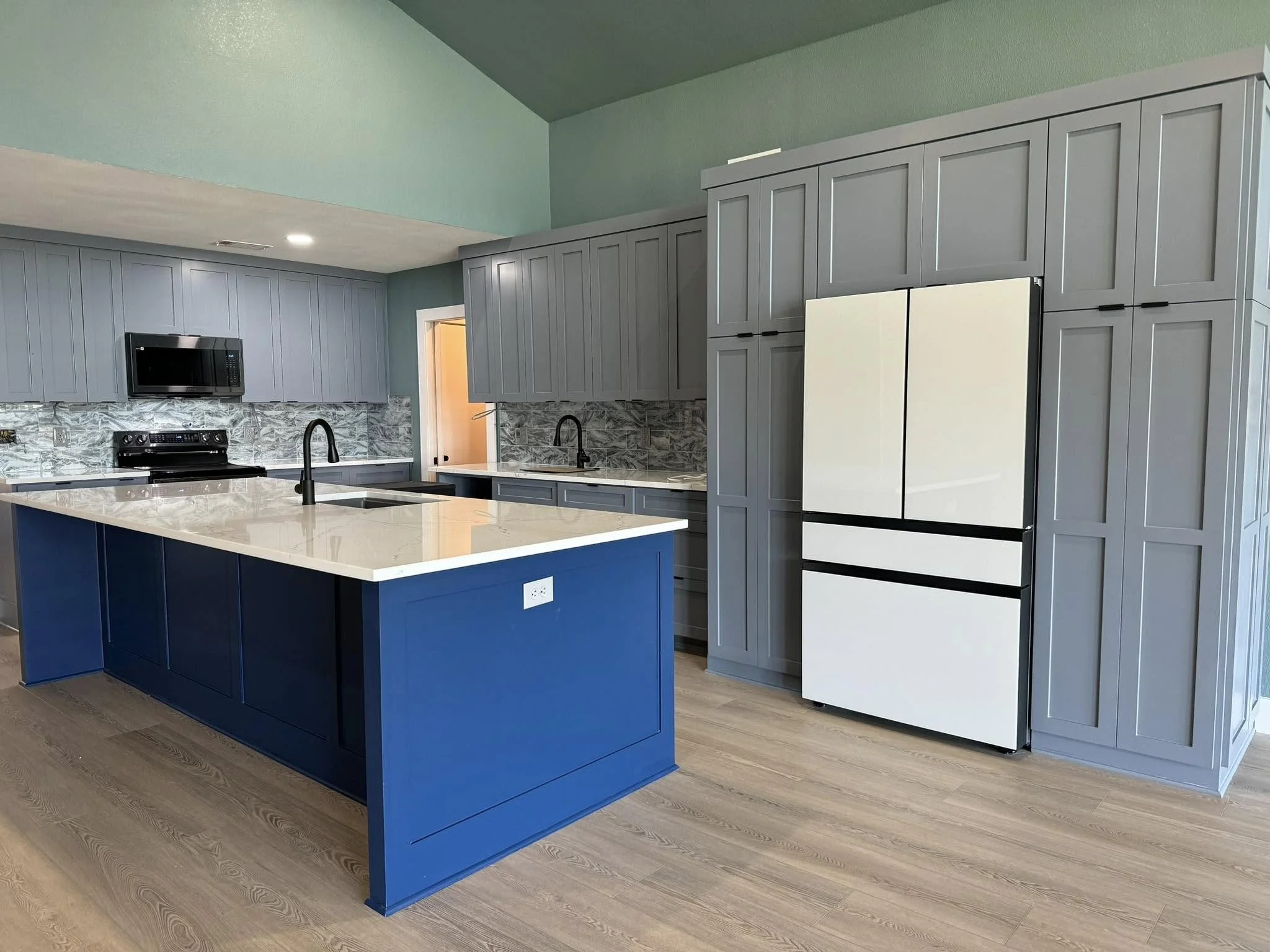 Modern kitchen with gray cabinets, a white island with a blue base, black fixtures, black appliances, and a gray marble backsplash.