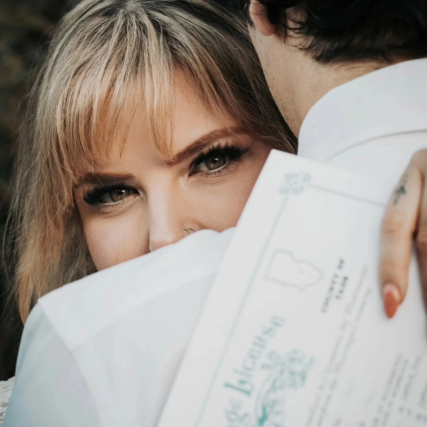Close up of a smiling blonde bride holding her marriage license in front of her face next to her groom in Lubbock Texas