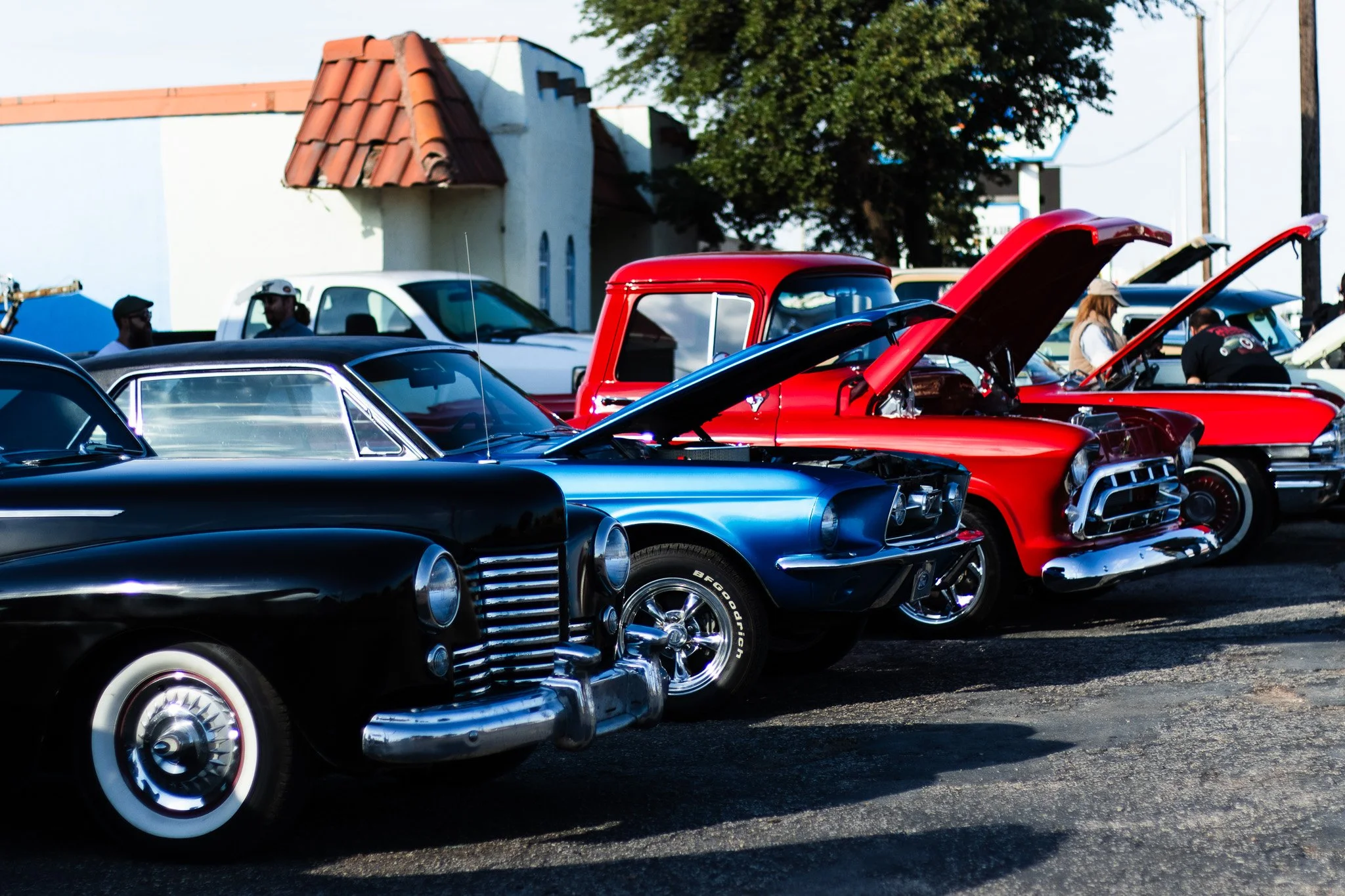 A wide angle view of a classic car show lineup featuring vintage automobiles with their hoods popped open on display in Midland Texas