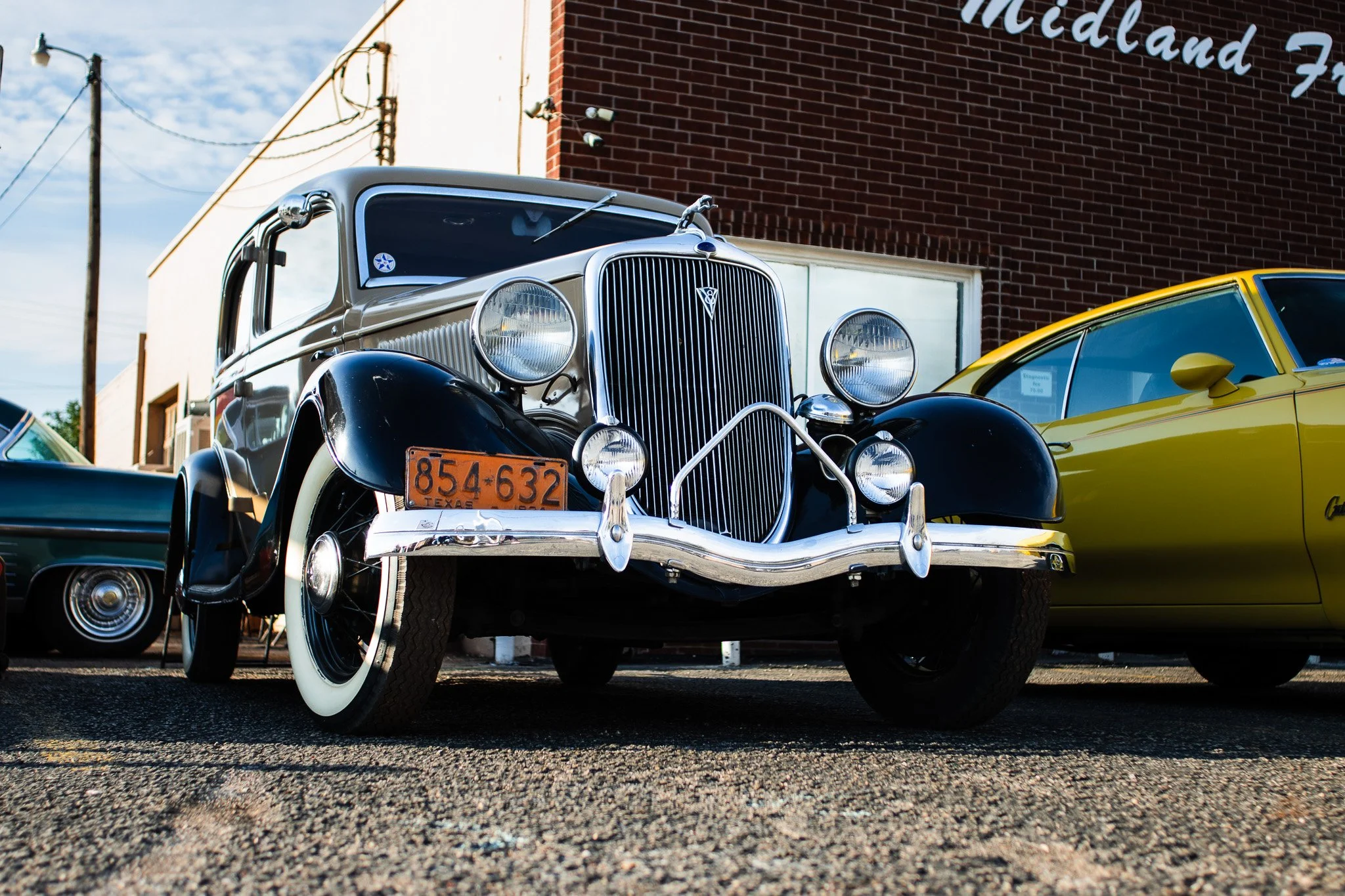 A classic black four-door vintage sedan parked on asphalt in front of a brick building in Midland Texas