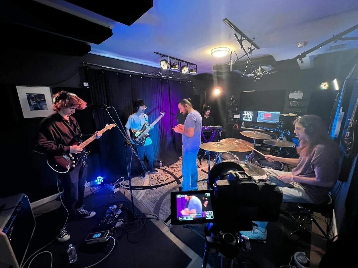 A live music performance setup inside a recording studio with a guitarist and keyboard player under dramatic blue stage lighting in Lubbock Texas